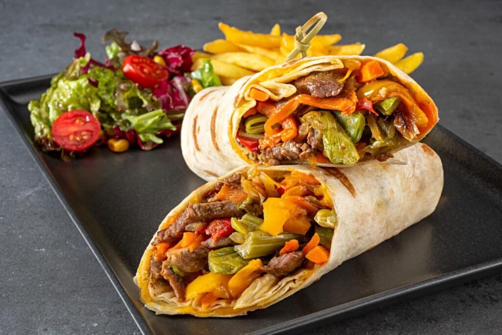 A variety of healthy high-protein wraps filled with grilled chicken, turkey, steak, tuna salad, and fresh vegetables arranged on a wooden table.